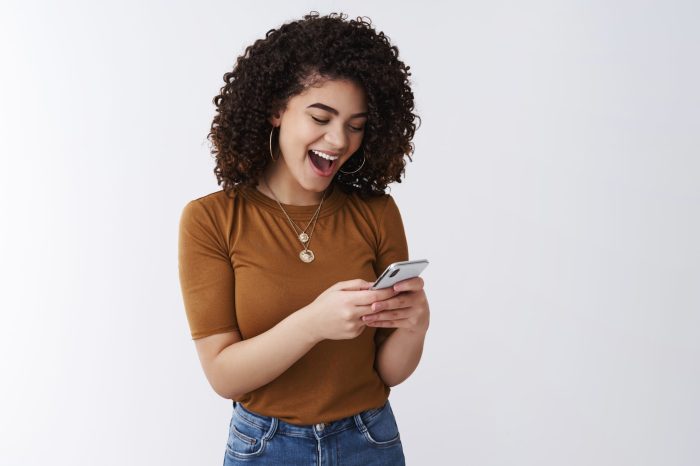So awesome simple. Cheerful attractive young relaxed curly dark hair stylish girl laughing open mouth excited reading daring message hold smartphone reacting amused funny video online look display.